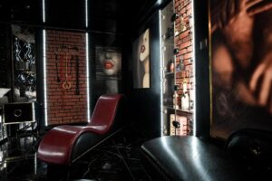 pokój z barkiem i obrazami kobiet na ścianach, na środku bordowa leżanka