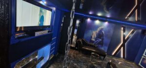 pokój z telewizorem i czarną kanapą, niebieskie ściany, duży obraz kobiety